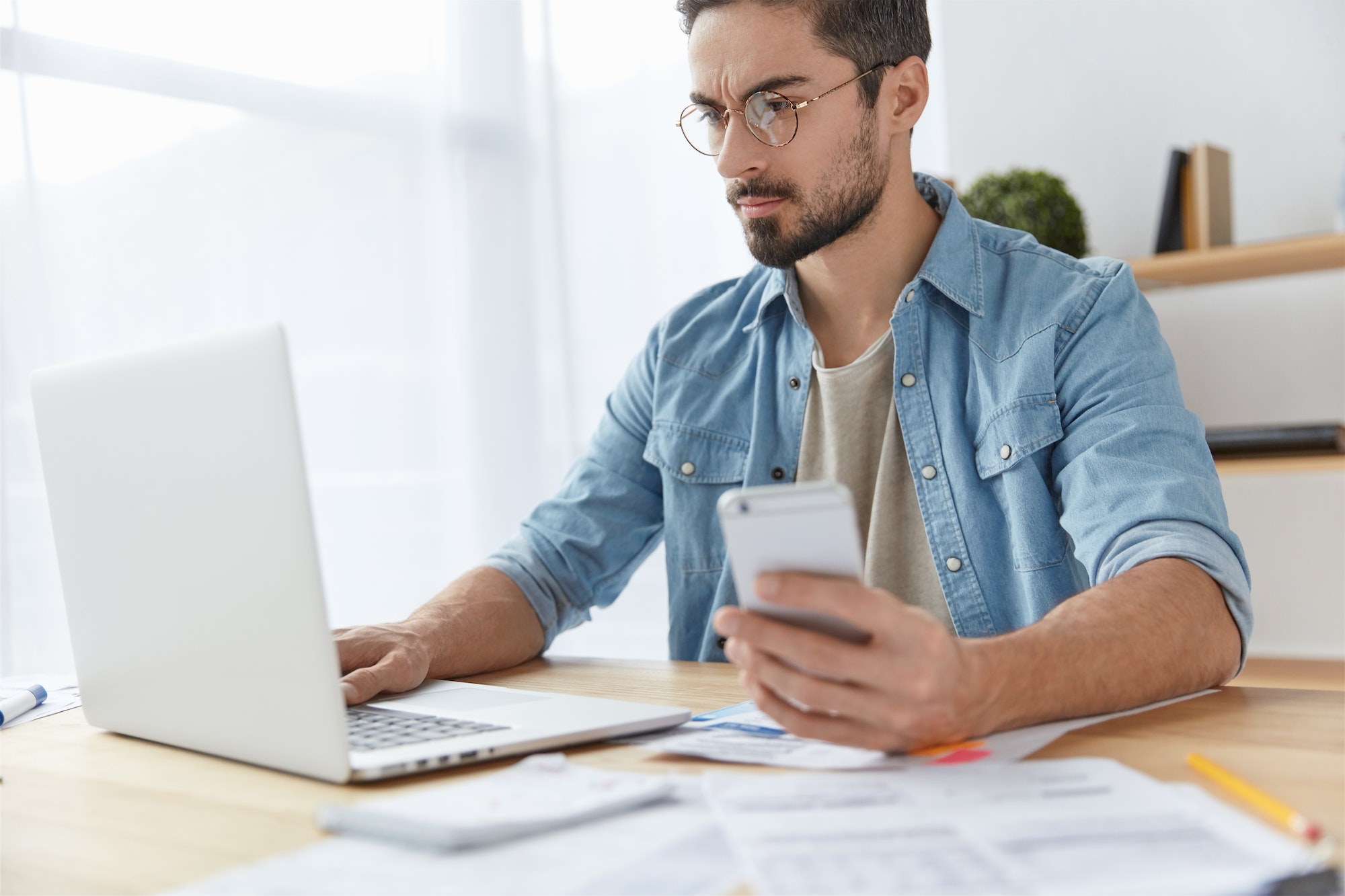 Successful young male freelancer with thick beard and mustache installs application for modern cell